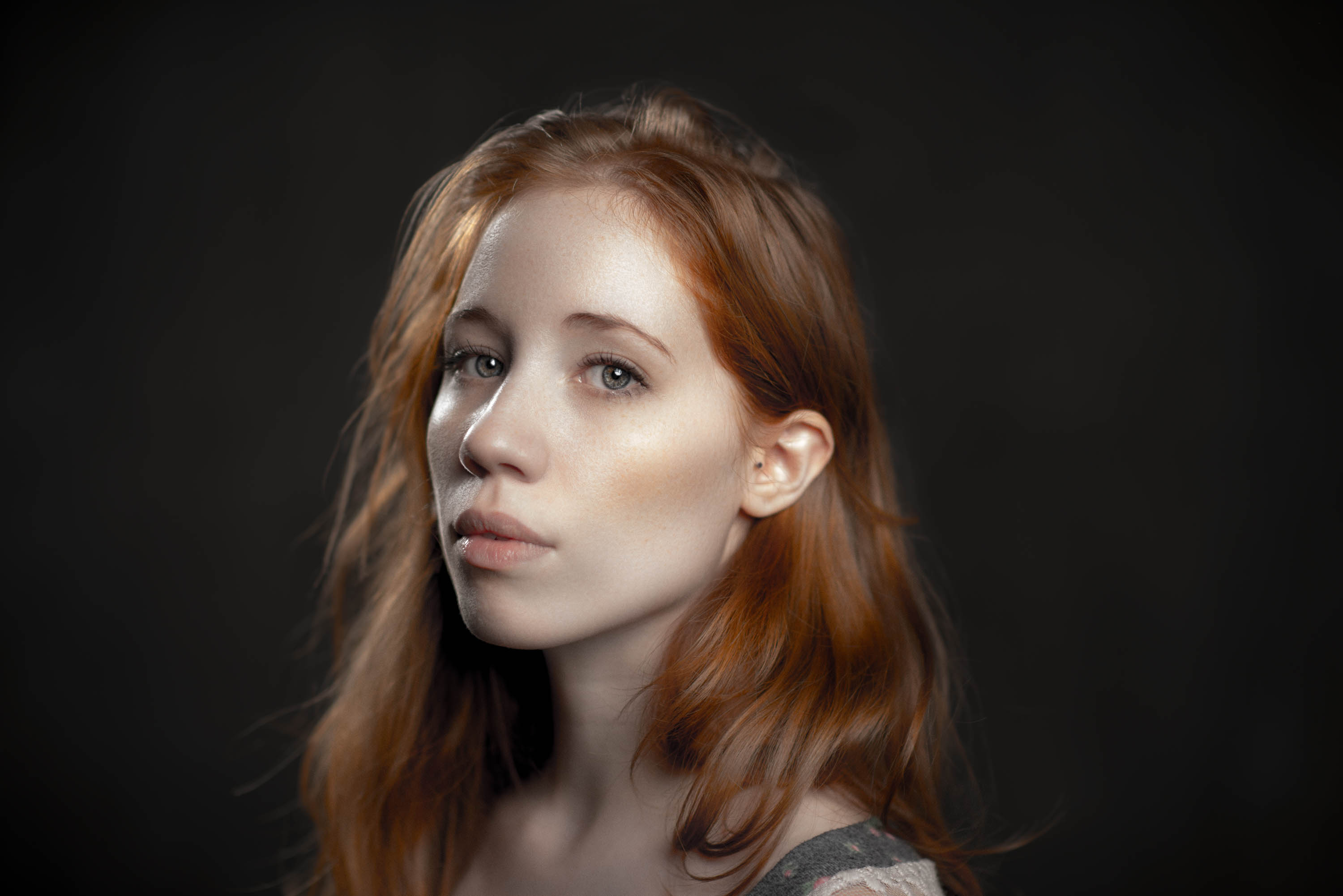 A painterly and warmly lit portrait of the face of a woman with auburn hair, pale skin, and bright blue eyes
