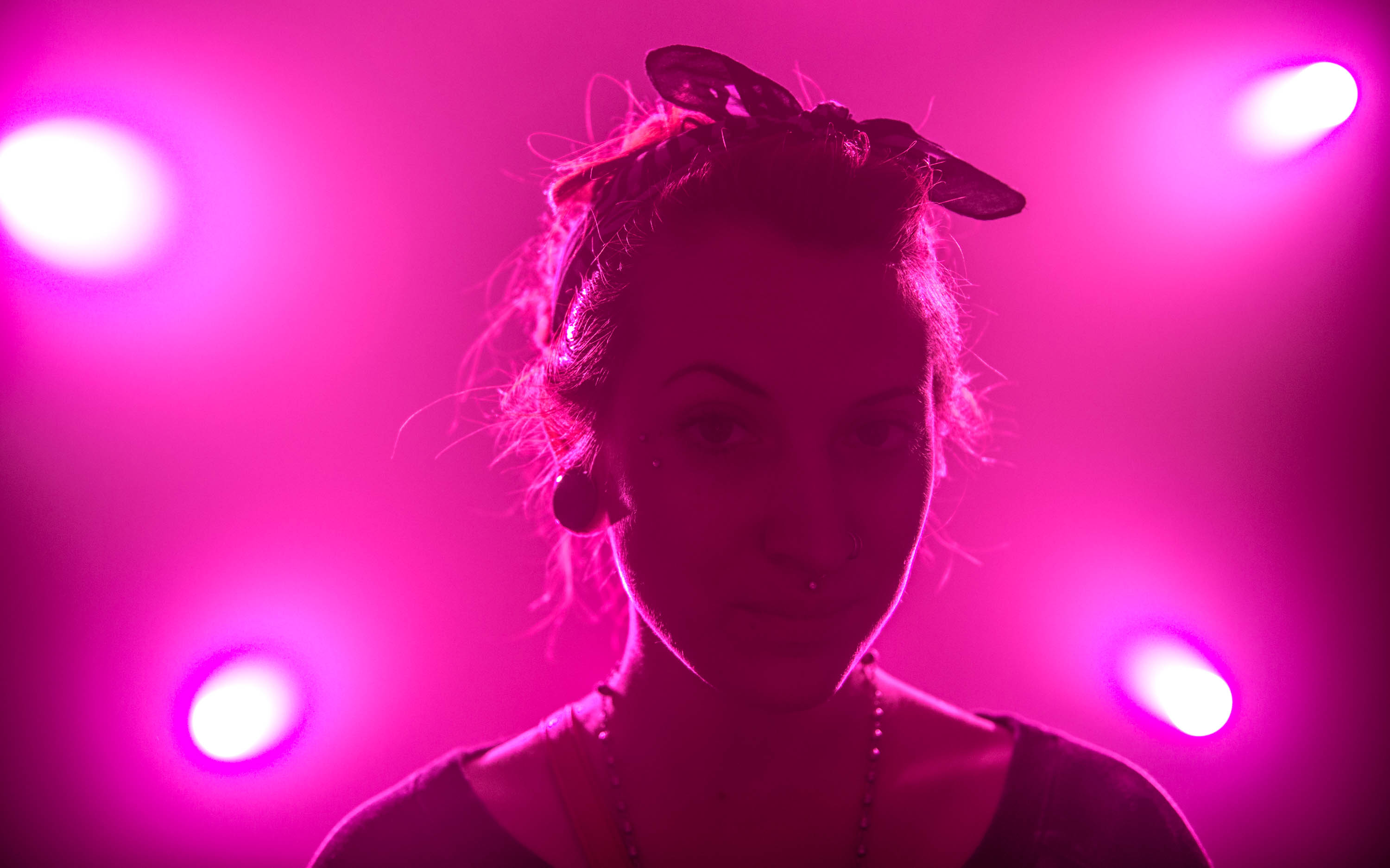 Portrait of a woman bathed in pink light, with her hair tied up in bandana and large plug earrings.